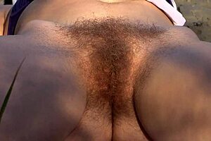 Outdoors by the river, this milf in swimsuit sunbathes with hairy pussy - wanna watch her amateur fingering close up?